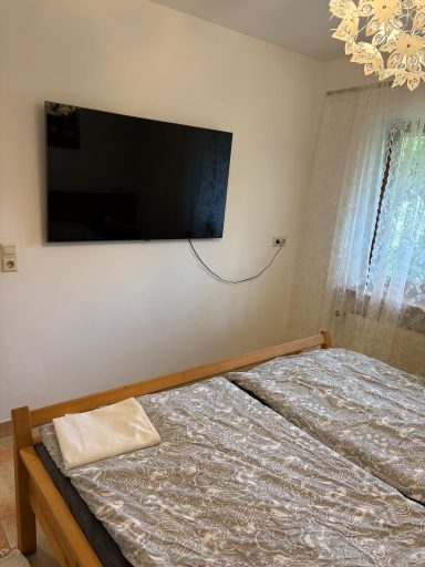 Schlafzimmer mit Doppelbett, flacher Fernseher an der Wand und Fenster mit Vorhängen.