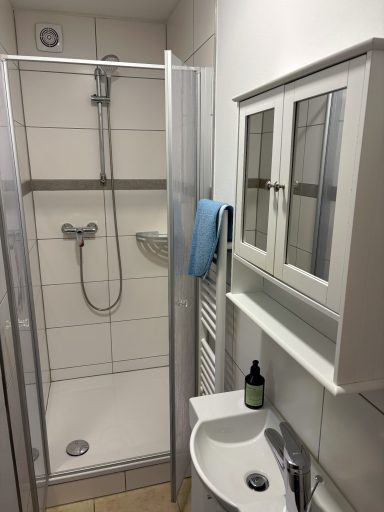 Moderne Dusche mit Glaswand, Waschbecken und Wandregal in einem hellen Badezimmer.