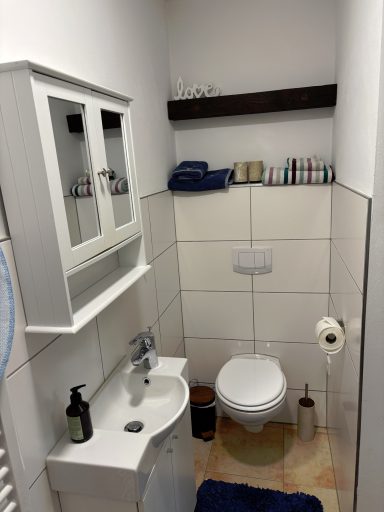 Kleines Badezimmer mit Toilette, Waschbecken und Regal an der Wand.