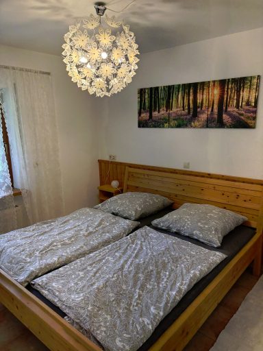 Schlafzimmer mit Holzbett, zwei Bettdecken und einer auffälligen Deckenleuchte.